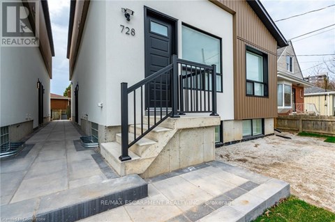 A modern house with a black door and a black railing on the stairs.