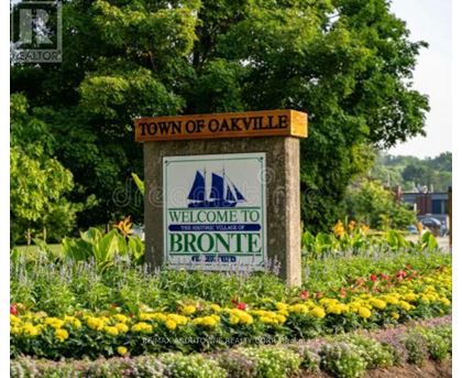 A sign that says "Town of Oakville Welcome to Bronte" is in front of some flowers.