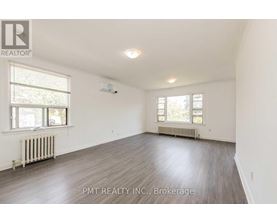 A spacious room with wood flooring and two windows.