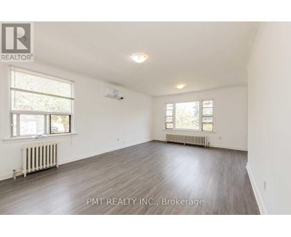A spacious room with wood flooring and two windows.
