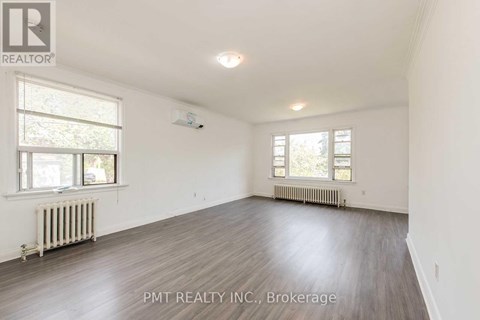 A spacious room with wood flooring and two windows.