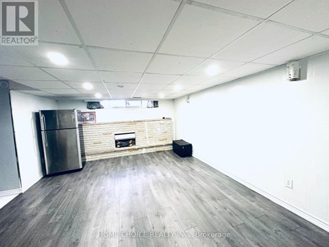 A spacious room with a wooden floor, a stainless steel refrigerator, and a fireplace.