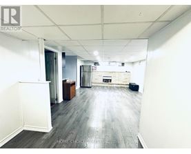 A spacious room with wooden flooring and white walls, featuring a kitchenette with a refrigerator, oven, and sink.