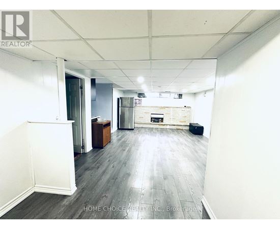 A spacious room with wooden flooring and white walls, featuring a kitchenette with a refrigerator, oven, and sink.