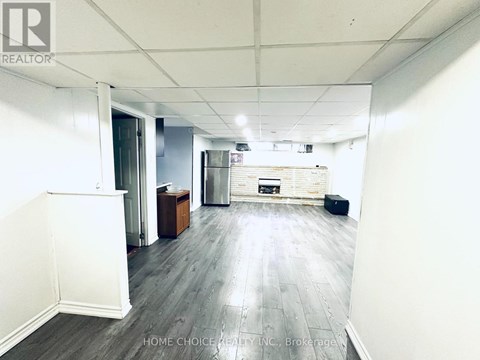 A spacious room with wooden flooring and white walls, featuring a kitchenette with a refrigerator, oven, and sink.