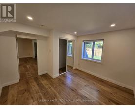 A room with wooden flooring and white walls, with a window showing a view of trees outside.