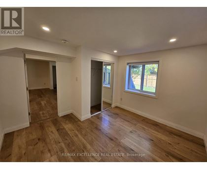 A room with wooden flooring and white walls, with a window showing a view of trees outside.