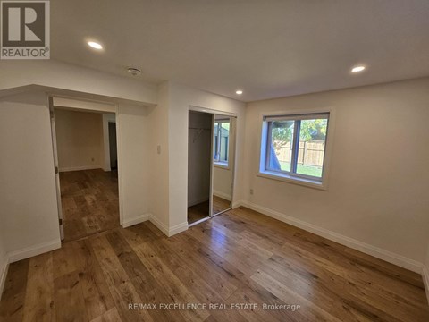 A room with wooden flooring and white walls, with a window showing a view of trees outside.