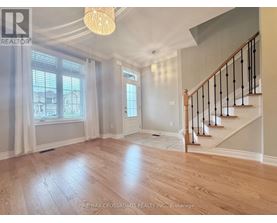 A well-lit, spacious room with wooden flooring and a staircase with black railings.