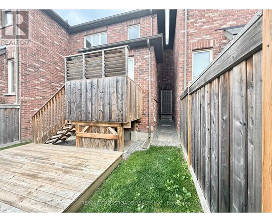 A wooden deck leads to a brick building with a wooden fence on the right.