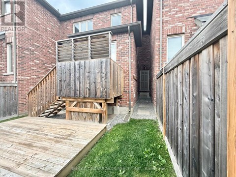 A wooden deck leads to a brick building with a wooden fence on the right.
