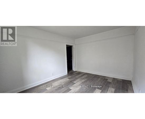 A room with a wooden floor and white walls, with a doorway leading to another room.