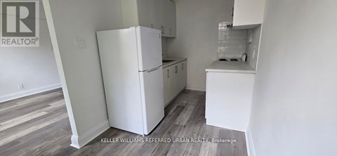 A white refrigerator in a kitchen with wooden floors.
