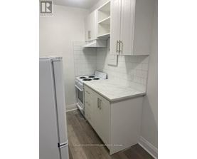A white kitchen with a refrigerator and a stove top oven.