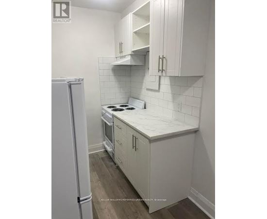 A white kitchen with a refrigerator and a stove top oven.