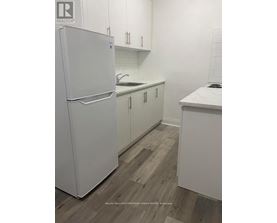A white refrigerator stands in a kitchen with white cabinets and a white counter.