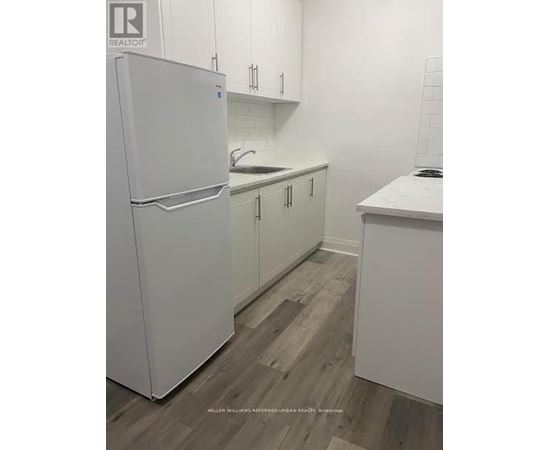 A white refrigerator stands in a kitchen with white cabinets and a white counter.