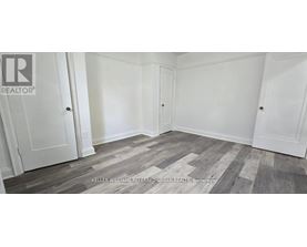 A room with white walls and wooden flooring with a REALTOR sign on the wall.