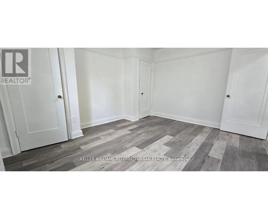 A room with white walls and wooden flooring with a REALTOR sign on the wall.