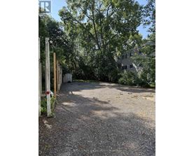 A gravel area with a wooden post and a building in the background.