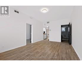 A room with wooden flooring and white walls, with a door on the right and a refrigerator in the middle.