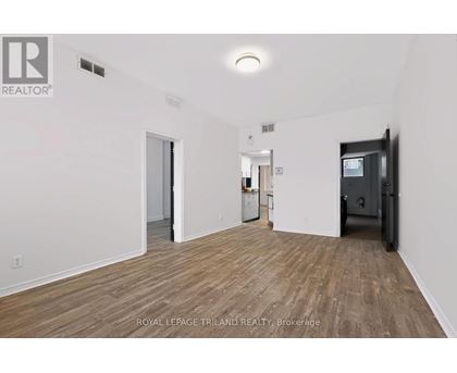 A room with wooden flooring and white walls, with a door on the right and a refrigerator in the middle.