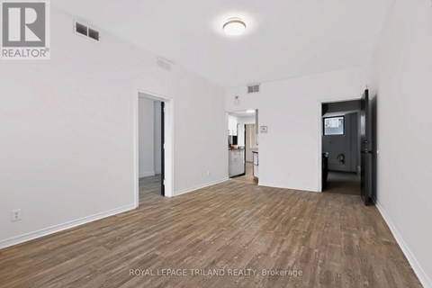 A room with wooden flooring and white walls, with a door on the right and a refrigerator in the middle.
