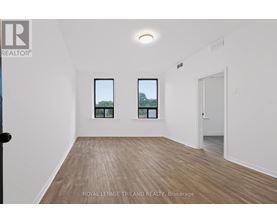 A room with wooden flooring and two windows showing trees outside.