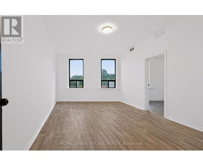 A room with wooden flooring and two windows showing trees outside.