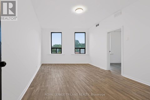 A room with wooden flooring and two windows showing trees outside.