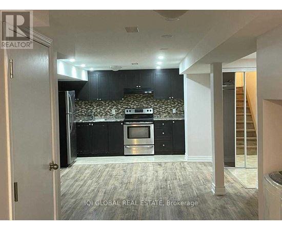 A kitchen with black cabinets and a patterned backsplash is visible from a hallway.