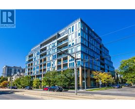 A modern multi-story building with a glass facade is situated on a street corner with cars parked along the curb.