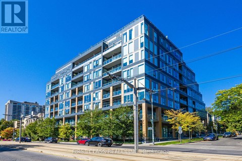 A modern multi-story building with a glass facade is situated on a street corner with cars parked along the curb.