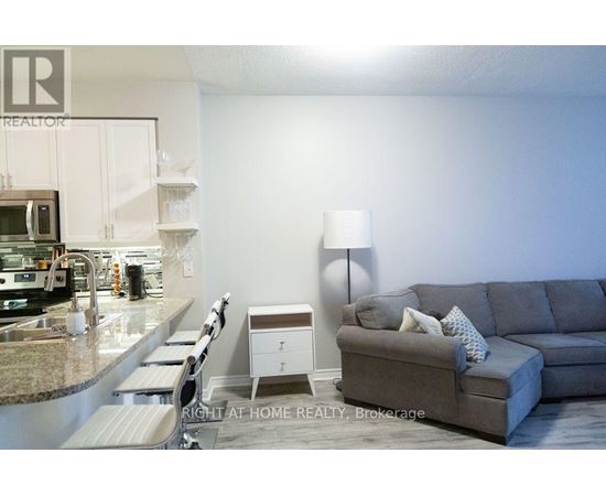 A grey couch with a white pillow is in the middle of a kitchen and living room.