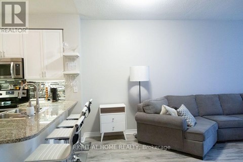 A grey couch with a white pillow is in the middle of a kitchen and living room.