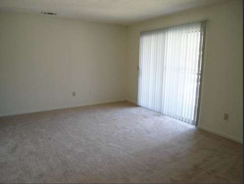A room with a carpeted floor and a window with blinds.