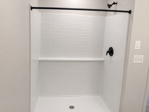 A white tiled bathroom with a black grab bar.