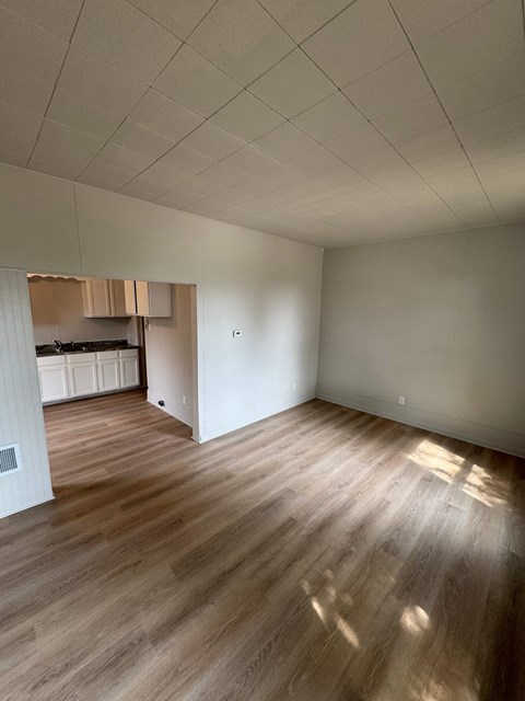 A room with wooden flooring and a kitchen in the background.