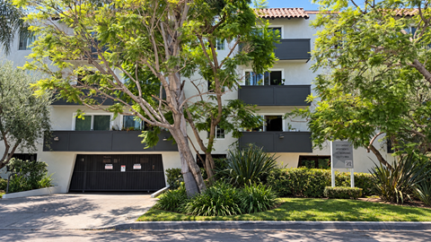 A modern building with a black garage door is surrounded by greenery.