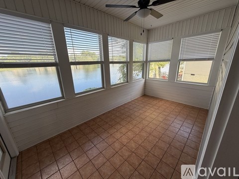 A room with a ceiling fan and large windows overlooking a body of water.