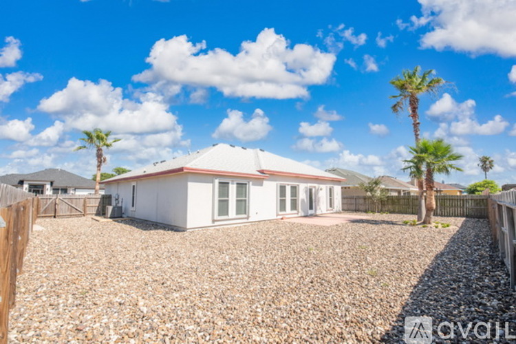 A house with a gravel yard and palm trees in the background.