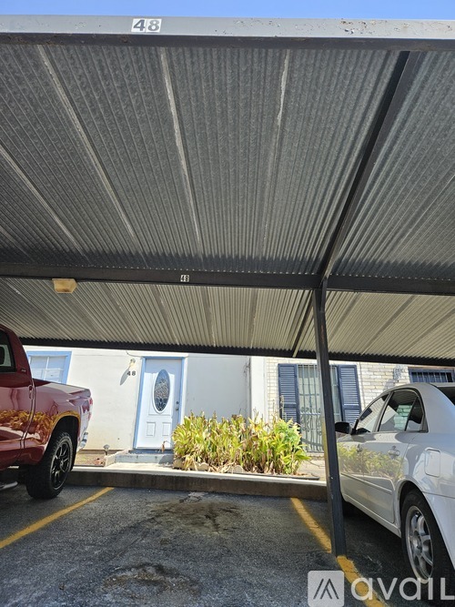 A parking area with a red truck and a white car under a corrugated metal roof.