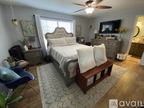 A well-lit bedroom with a large bed, a blue chair, and a ceiling fan.