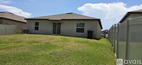A house with a brown roof and a grey exterior is surrounded by a fence.