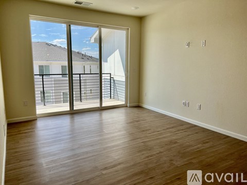 Empty room with wooden flooring and sliding glass doors.
