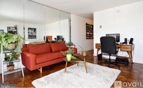 A living room with a red couch, a white rug, and a wooden desk.