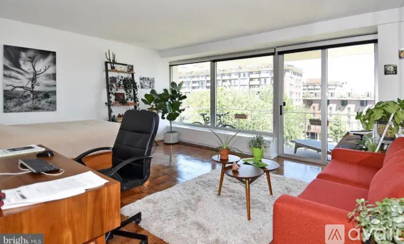 A living room with a red couch, a wooden desk, and a large window overlooking a cityscape.