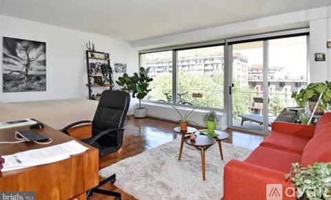 A living room with a red couch, a wooden desk, and a large window overlooking a cityscape.