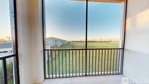 A balcony with a metal railing and a view of a grassy area and buildings.