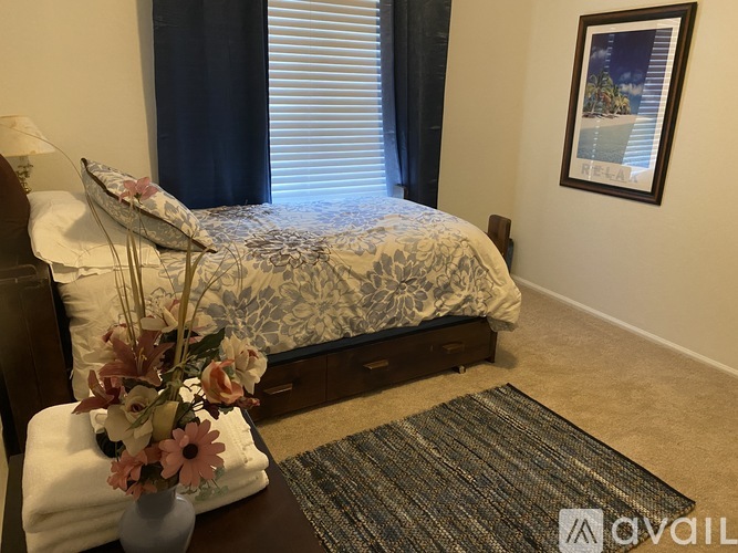 A bedroom with a bed, a vase with flowers, and a picture on the wall.